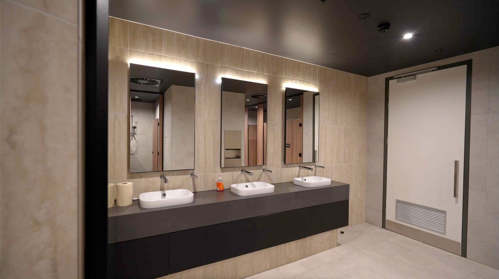 East Edge 2 premium bathroom amenities - triple vanity with backlit mirrors, dark stone benchtop and marble-style wall tiles
