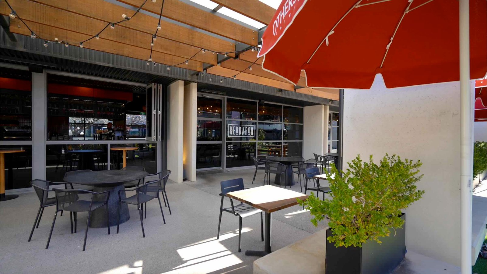 Red Baron cafÃ© outdoor terrace at East Edge 2 - covered pergola with festoon lights and precinct views
